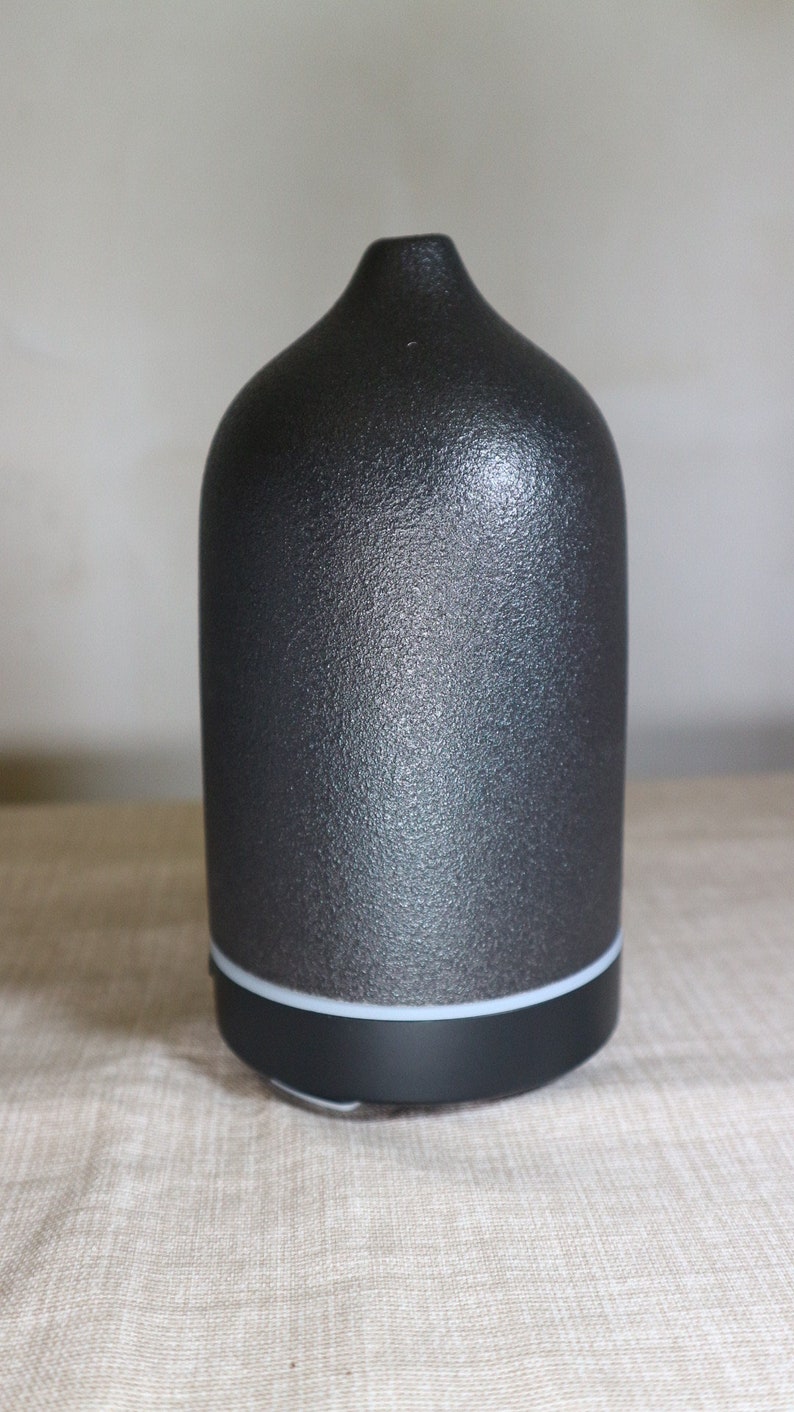 May include: A black ceramic essential oil diffuser with a textured finish. The diffuser has a white ring around the base.