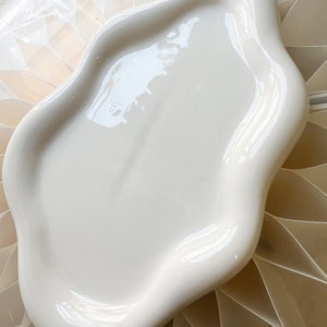 May include: A white ceramic serving tray with a wavy, organic shape. The tray is smooth and glossy.