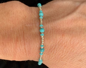 May include: A turquoise and silver beaded bracelet on a person's wrist.