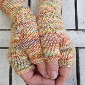Könnte beinhalten: Ein Paar Fingerlose Handschuhe, gestrickt aus einem mehrfarbigen Garn mit einem gestreiften Muster. Die Handschuhe sind eine Mischung aus Pfirsich, Gelb und Grün.