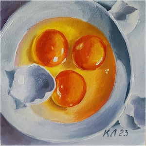 May include: A close-up of three egg yolks in a white bowl. The yolks are a vibrant orange colour and are surrounded by a clear, yellow liquid. The bowl is sitting on a white surface.