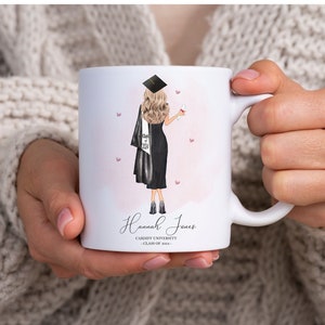 May include: White ceramic mug with a pink and white watercolor background. A cartoon illustration of a woman wearing a black graduation gown and cap, holding a diploma. The text "Hannah Jones" is printed below the illustration, along with "Cardiff University - Class of 2024".