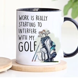 May include: White ceramic coffee mug with a black rim and handle. The mug features a black and white graphic of a golf bag with clubs and the text "Work is really starting to interfere with my golf."
