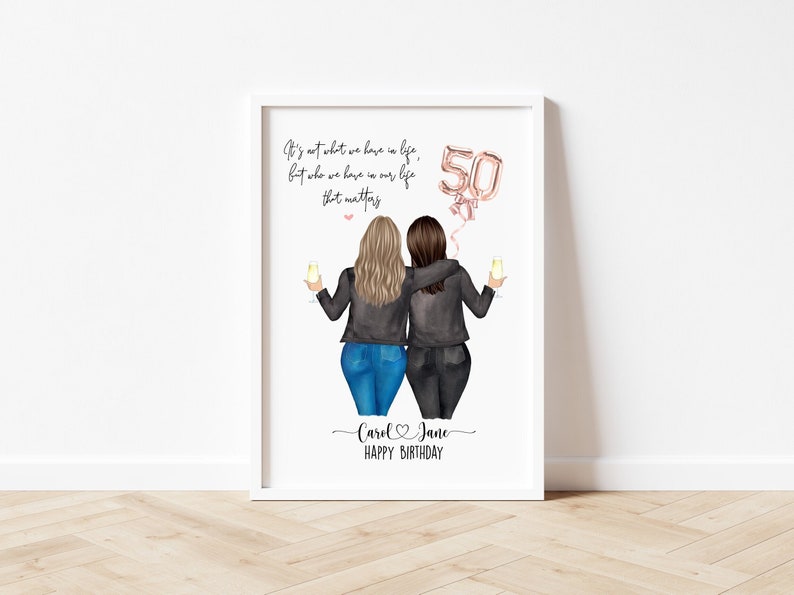 May include: A white framed print with a quote about friendship and a drawing of two women in black jackets and jeans, holding glasses of champagne. The quote reads "It's not what we have in life, but who we have in our life that matters." There is a pink and gold balloon that says "50" and the names "Carol & Jane" with the text "Happy Birthday" below.