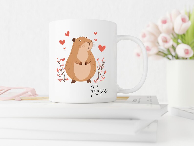 Puede incluir: Taza de cer&aacute;mica blanca con un h&aacute;mster de dibujos animados marr&oacute;n con corazones rosas y el nombre "Rosie" impreso en la taza.