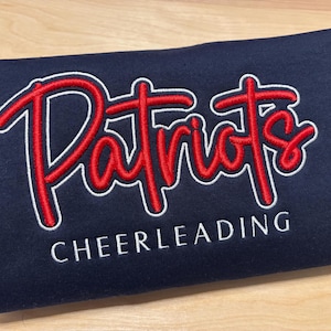 May include: Navy blue sweatshirt with white and red embroidered text that reads "Patriots Cheerleading".