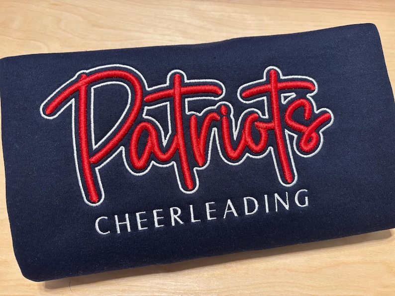 May include: Navy blue sweatshirt with white and red embroidered text that reads "Patriots Cheerleading".