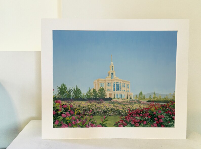 May include: An oil painting of a light-colored building with a tall spire, set against a blue sky. The building is surrounded by green trees and a vibrant garden of pink and red flowers. The artwork is framed in white.