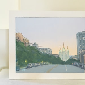 May include: A painting of a city street scene with a view of the Salt Lake Temple in the distance. The street is lined with trees and cars, and the sky is a soft blue.