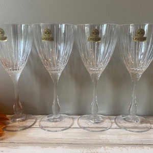 May include: Four clear glass wine glasses with a decorative etched pattern. Each glass has a gold label that reads "RCR Oneida".