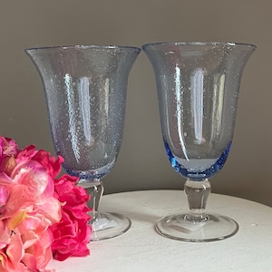 May include: Two clear glass goblets with a blue rim and a textured surface. The goblets have a round base and a flared top.