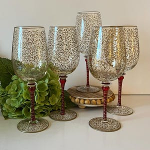 May include: Set of five clear glass wine glasses with a gold filigree design and red stems.