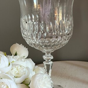 Puede incluir: Una copa de cristal tallado transparente con un cuenco en forma de tulip&aacute;n y un tallo detallado. El cristal tiene un patr&oacute;n texturizado y se asienta sobre una base redonda. Flores blancas dispuestas cerca de la copa.