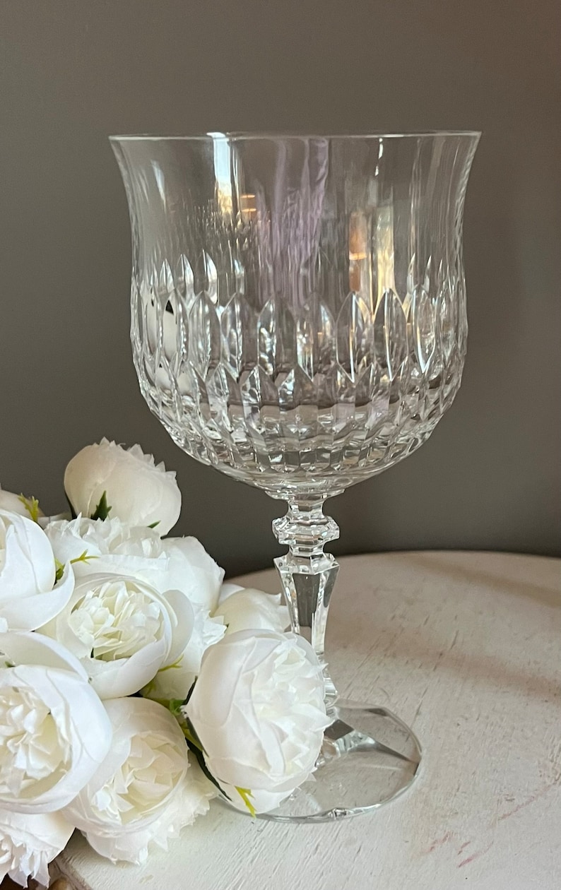 Puede incluir: Una copa de cristal tallado transparente con un cuenco en forma de tulip&aacute;n y un tallo detallado. El cristal tiene un patr&oacute;n texturizado y se asienta sobre una base redonda. Flores blancas dispuestas cerca de la copa.