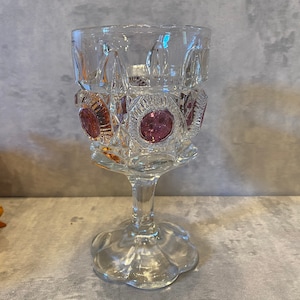 May include: A clear glass goblet with a cut glass design and pink and amber colored glass accents. The goblet has a wide base and a tall stem.