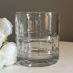K&ouml;nnte beinhalten: Ein klarer Glasbecher mit quadratischem Muster. Das Glas ist leer und hat eine glatte, polierte Oberfl&auml;che.