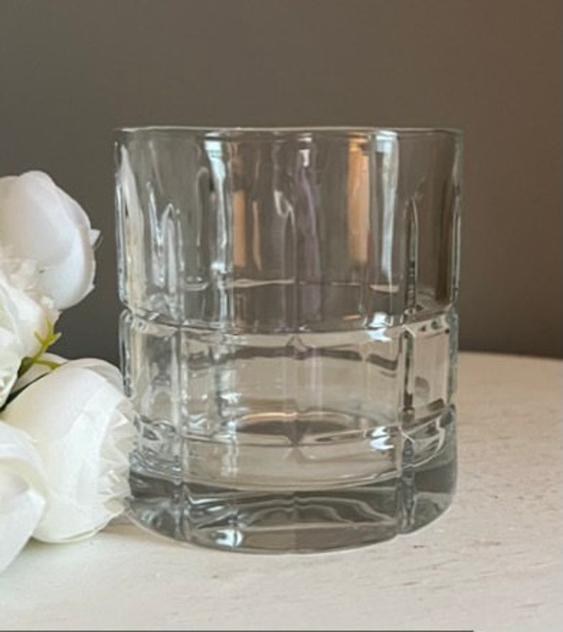 K&ouml;nnte beinhalten: Ein klarer Glasbecher mit quadratischem Muster. Das Glas ist leer und hat eine glatte, polierte Oberfl&auml;che.