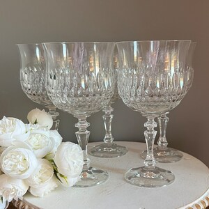 Puede incluir: Cuatro copas de vino de cristal transparente con intrincados patrones tallados. Las copas tienen un cuenco en forma de tulip&aacute;n, un tallo delgado y una base redonda. Flores blancas en primer plano a&ntilde;aden elegancia.
