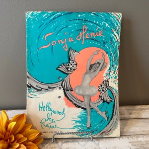 May include: A vintage program for the Hollywood Ice Review featuring Sonja Henie. The cover features a colorful illustration of a woman ice skating in a white tutu and pink leotard against a turquoise and pink background.