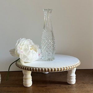 May include: White wooden pedestal with three legs and a gold beaded trim. A clear glass vase with a textured surface sits on top of the pedestal.