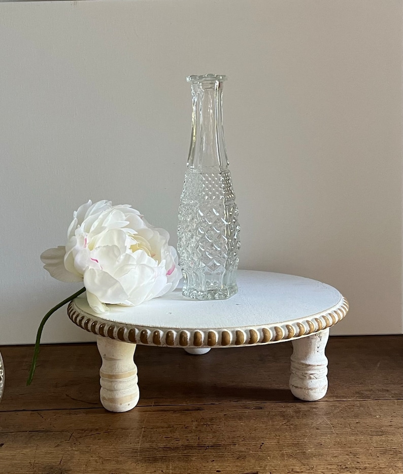 May include: White wooden pedestal with three legs and a gold beaded trim. A clear glass vase with a textured surface sits on top of the pedestal.