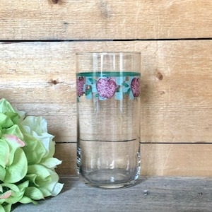 May include: A clear glass drinking glass with a green and pink apple design around the middle.