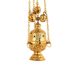 May include: A gold-colored censer with intricate floral patterns and a bell-shaped design. The censer is suspended by gold chains and features small bells at the top. The ornate details and polished finish suggest a religious or ceremonial purpose.
