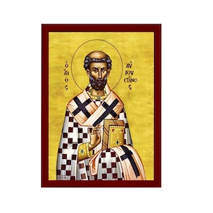 May include: A Byzantine icon of Saint Anthony the Great, depicted in a traditional style with a gold background. He is wearing a white and red checkered robe and holding a book. The text on the icon reads "Άγιος Αντώνιος".