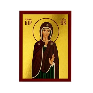 Puede incluir: Un icono de la Virgen María con fondo dorado y marco rojo. Lleva una túnica burdeos y una prenda interior verde. Su mano derecha está levantada a sus labios y su mano izquierda está levantada en un gesto de bendición. El icono está inscrito con el texto "ΟΧΙ" y "ΤΗΡ".