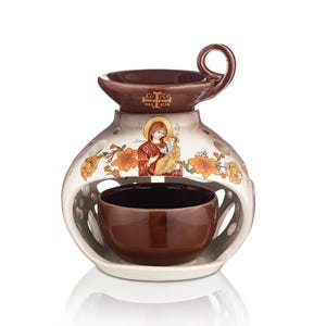 Op de afbeelding: Een crèmekleurige keramische oliebrander met een bruine bovenkant en handvat. Het heeft oranje bloemmotieven en een religieuze afbeelding. Een bruine kom staat erin.