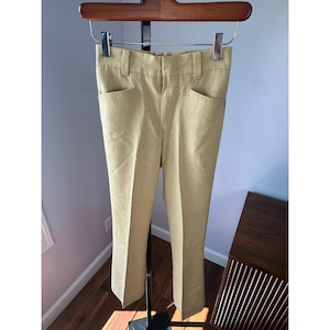 Può includere: Pantaloni color beige con un design a gamba dritta. I pantaloni hanno due tasche anteriori e passanti per la cintura. I pantaloni sono appesi a una gruccia di legno.