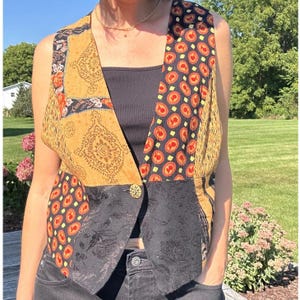 May include: A patchwork vest with a variety of patterns and colors. The vest features a mix of fabrics, including a mustard yellow paisley, black floral, and a pattern of red circles on a navy background. It has a gold button closure.