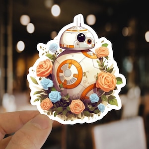 May include: A white and orange robot character with a round body and a single eye surrounded by a floral arrangement of peach and blue flowers.