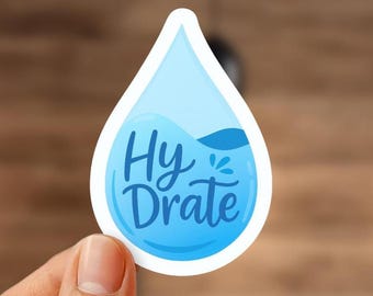 May include: A water droplet-shaped sticker with the words "Hy-Drate" in blue script. The sticker has a white border and a light blue interior with a darker blue wave graphic. The sticker is held by a hand.