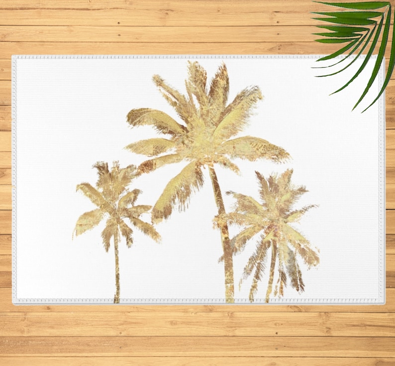 Three gold colored palm trees on a white background throw rug. The palm trees are stylized and have a watercolor effect. The palm trees are arranged in a staggered formation with the tallest palm tree in the center.