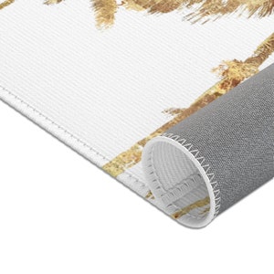May include: A white rug with a pattern of gold palm trees. The rug has a gray backing and is rolled up.