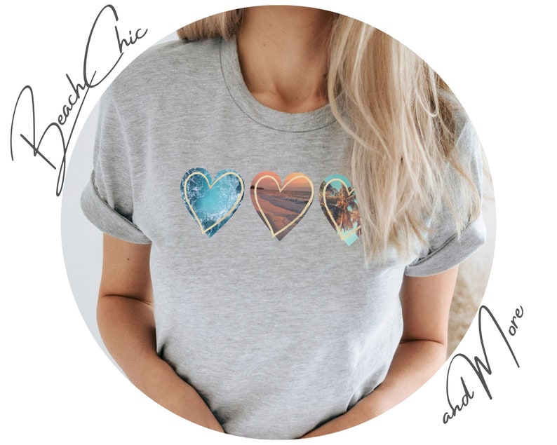 A gray t-shirt with three hearts printed on the front. Each heart has a different beach scene inside. The first heart has a blue ocean scene, the second heart has a sunset scene, and the third heart has a palm tree scene.