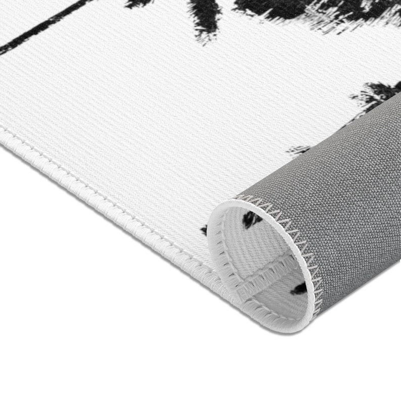 Peut inclure: Un tapis blanc avec un motif de palmier noir. Le tapis a un dos gris et est pli&eacute; pour montrer le dos.