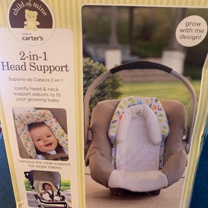 May include: A box for a 2-in-1 baby head support. The box is yellow with brown stripes and features a cartoon baby bear. The product is made by Carter's and is designed to grow with the baby. The box shows a baby in a car seat using the head support. The text on the box reads 'child of mine', 'made by carter's', '2-in-1 Head Support', 'Soporte de Cabeza 2 en 1', 'comfy head & neck support adjusts to fit your growing baby', 'remove the inner support for larger babies', 'perfect for car seats, strollers, bouncers & joggers', 'grow with me design!' and 'surround your little one in comfort'.