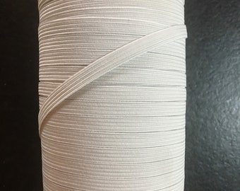 May include: A spool of white elastic cord wound around a cardboard tube. The elastic cord is thin and has a smooth texture.