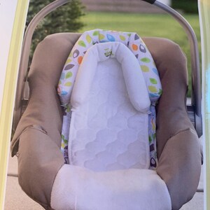 May include: A brown and white baby car seat with a white and green leaf patterned headrest and a white quilted insert.