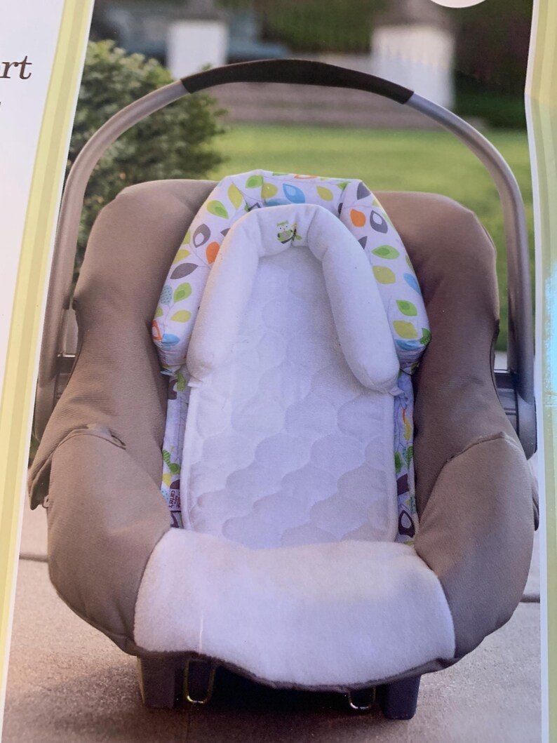 May include: A brown and white baby car seat with a white and green leaf patterned headrest and a white quilted insert.
