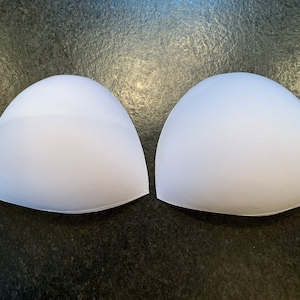 May include: Two white foam bra cups, commonly used for adding volume or shaping to a bra.