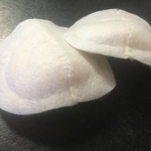 Könnte beinhalten: Zwei weiße Filzpolster, an den Rändern vernäht, zur Verwendung in Kleidung oder Bastelarbeiten.