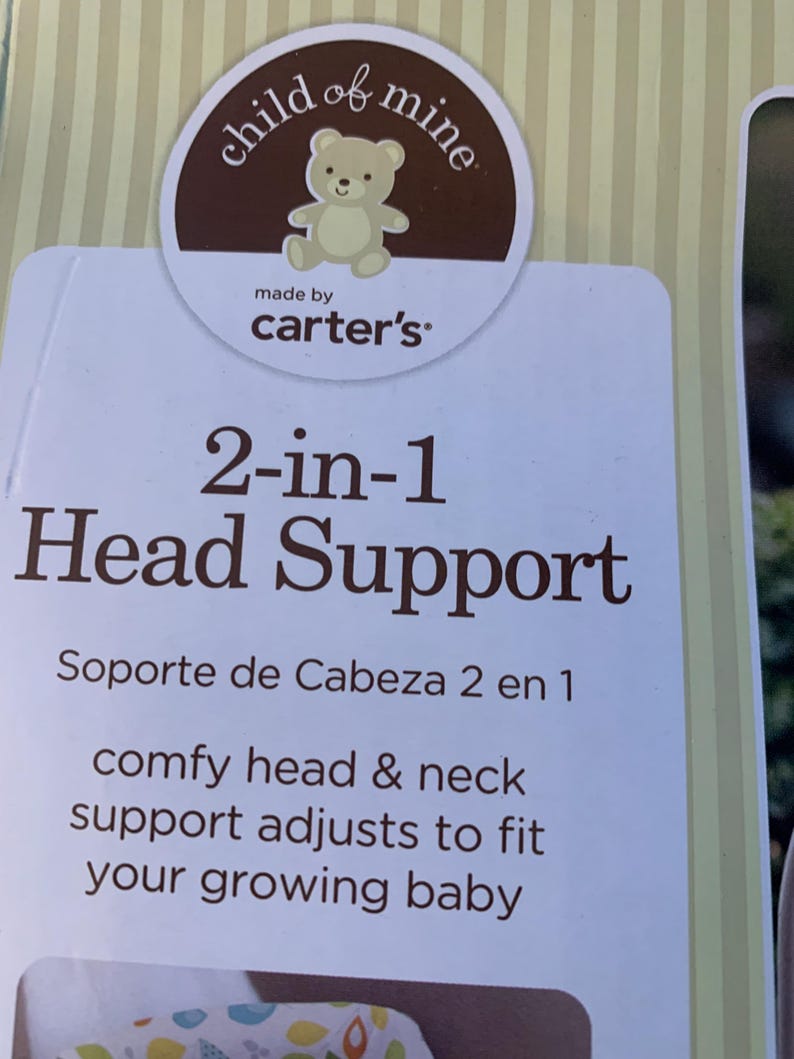 May include: A white and brown package for a 2-in-1 head support for babies. The package has a brown circle with the words 'child of mine' and 'made by carter's' in white text. The package also has the text '2-in-1 Head Support' in brown text and 'Soporte de Cabeza 2 en 1' in smaller brown text. The text 'comfy head & neck support adjusts to fit your growing baby' is also in brown text.