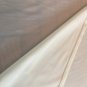May include: A white sheer fabric with a textured pattern. The fabric is folded in half, revealing a white, ribbed fabric underneath.