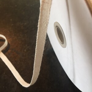 May include: A spool of off-white cotton twill tape. The tape is wound around a white cardboard spool with a hole in the center. The tape is about 1/2 inch wide.