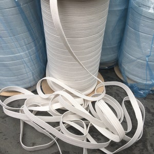 May include: White elastic cord wound on spools, with a loose end of the cord lying on a gray surface.