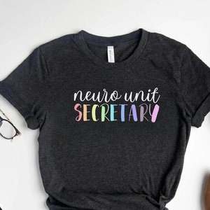 May include: Dark heather grey t-shirt with the text "neuro unit SECRETARY" in rainbow colors.