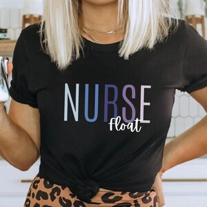 Könnte beinhalten: Schwarzes T-Shirt mit dem Text "NURSE float" in einem Farbverlauf von Blau und Lila. Das Wort "Black" ist in Kursivschrift unten rechts geschrieben. Eine Person hält eine silber-schwarze Tasse.